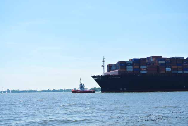 Schlepper zieht Containerschiff in den Hafen